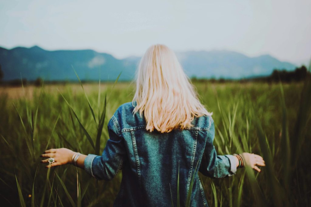 Blonde woman in denim surrounded by lush countryside in Ohlstadt, Germany. Serene and natural.